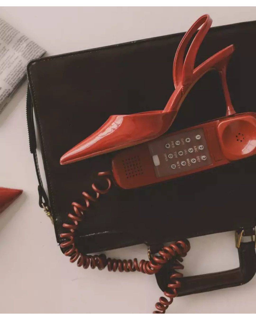 Red stiletto heel on leather briefcase with vintage phone — The details make the design